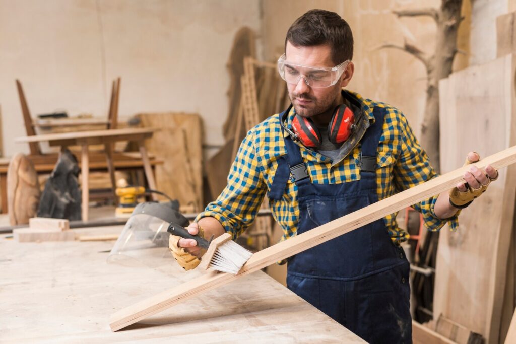 craftsman in a workshop applies paint to a wooden plank