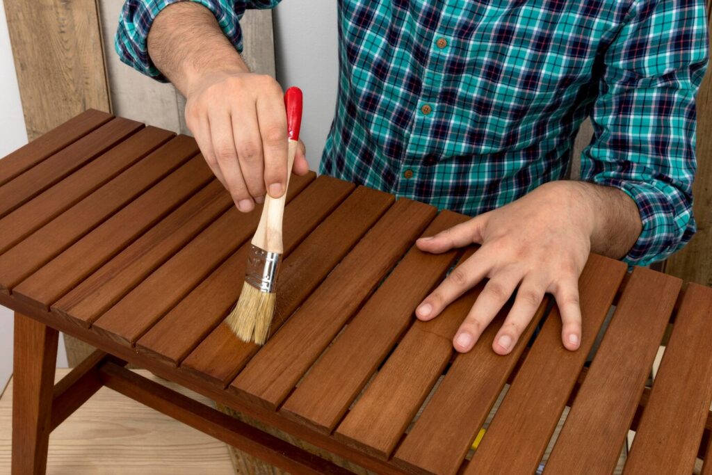 person in a plaid shirt brushes wood stain onto a wooden table