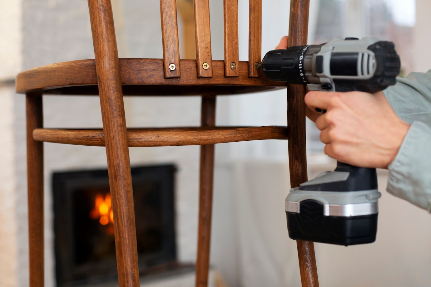 person uses a cordless drill to tighten screws on a wooden chair