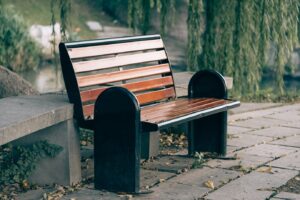 wooden bench with black armrests sits beside a creek