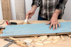 person applying blue paint to a wooden plank