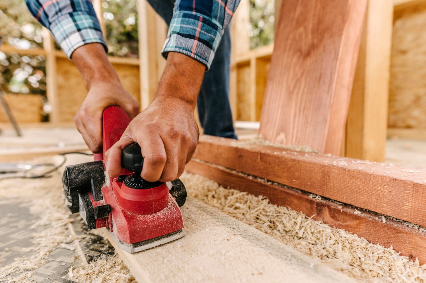 close-up of a person using a red electric planer on a wooden board