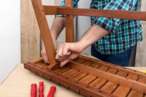 person in a plaid shirt tightens a screw on a wooden chair frame