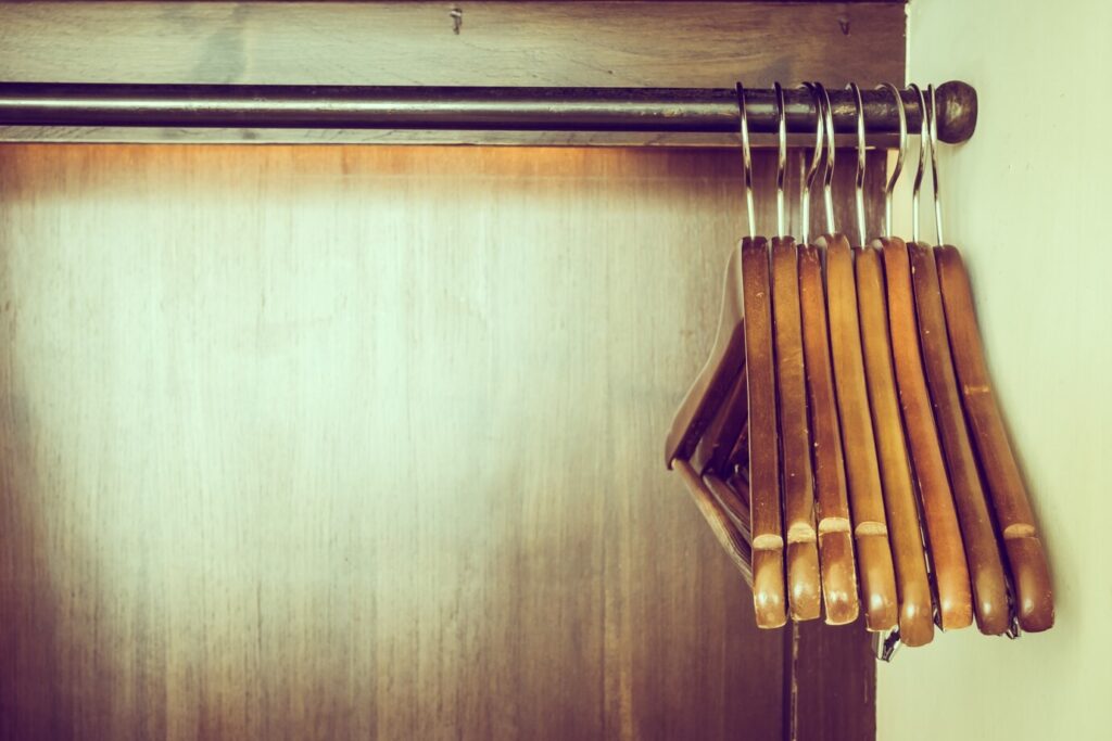 series of wooden hangers suspended on a metal rod against a warm-toned