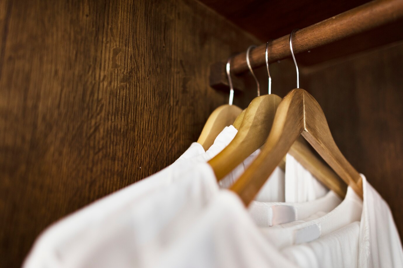 Several white shirts hang neatly on wooden hangers