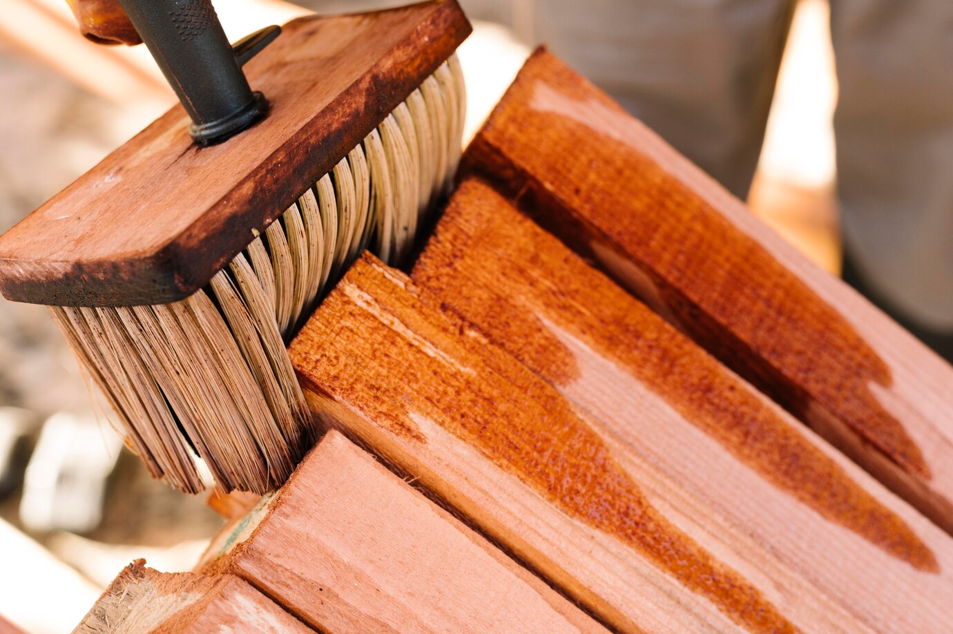 close-up of a wooden brush applying a reddish stain to planks of wood