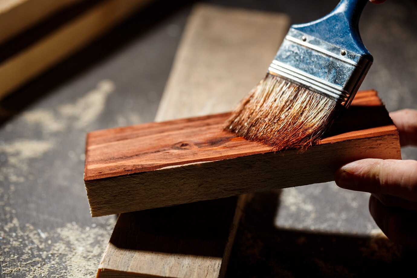 hand applies varnish to a wooden plank using a brush