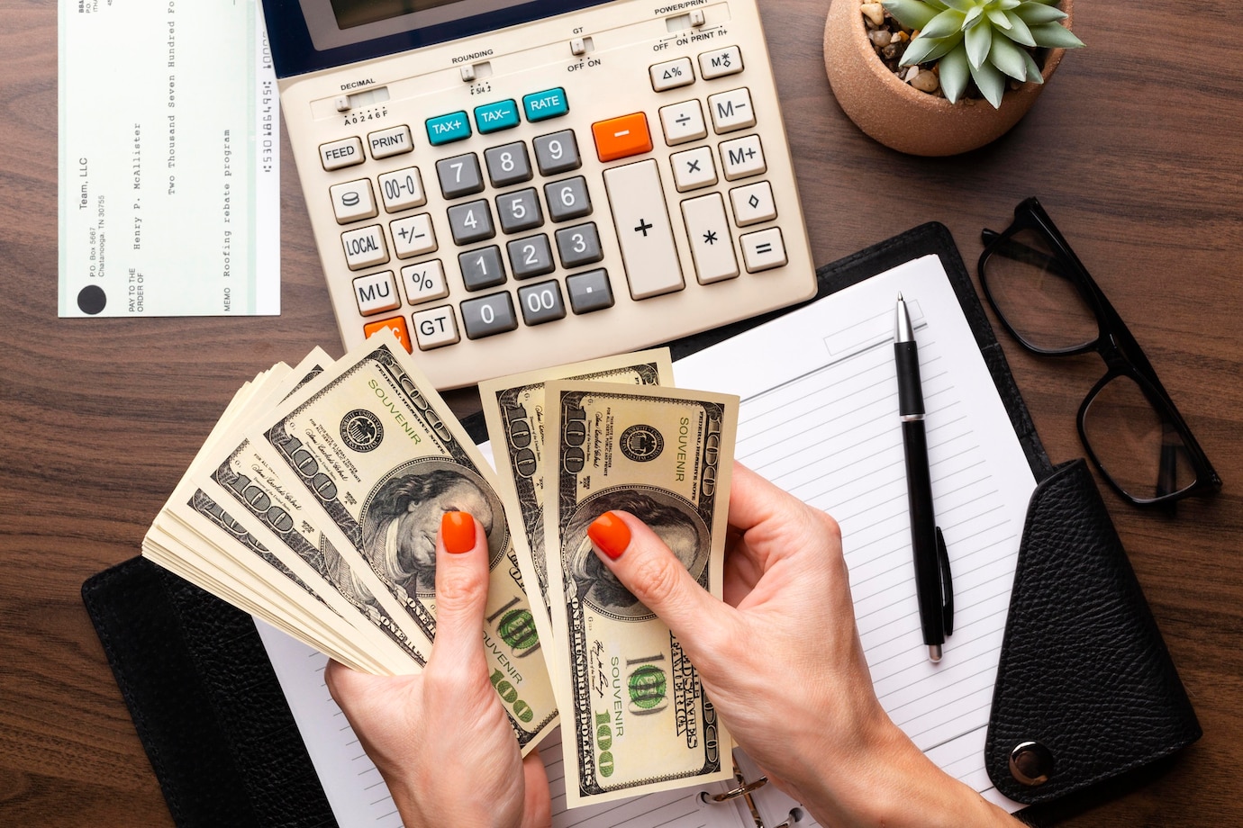 pair of hands holding cash and using a calculator, with a notepad