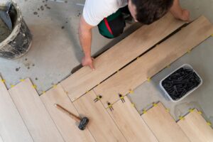 worker lays wooden flooring planks, using spacers and a mallet