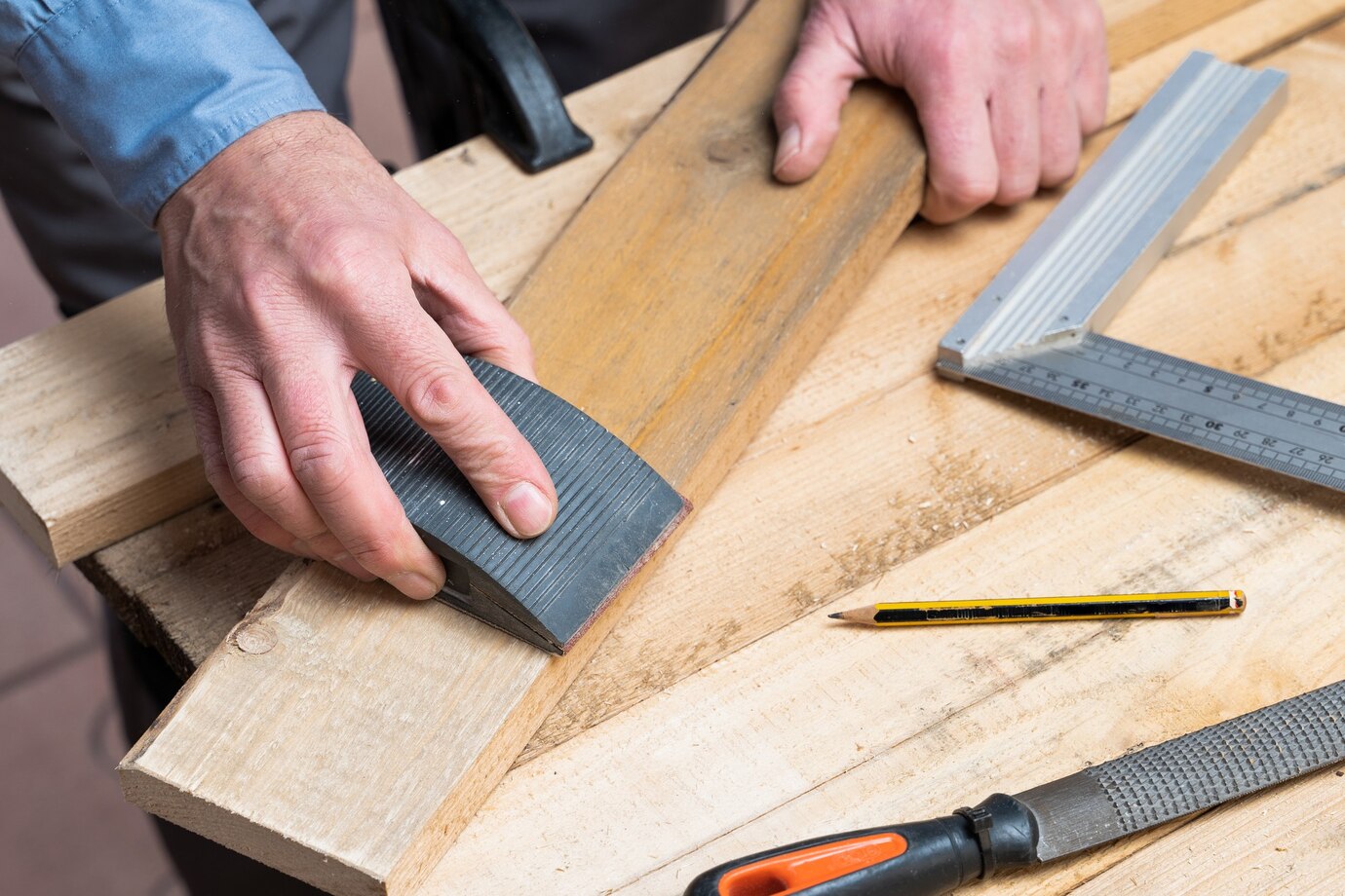 hand using a hand plane on a wooden board with measuring tools
