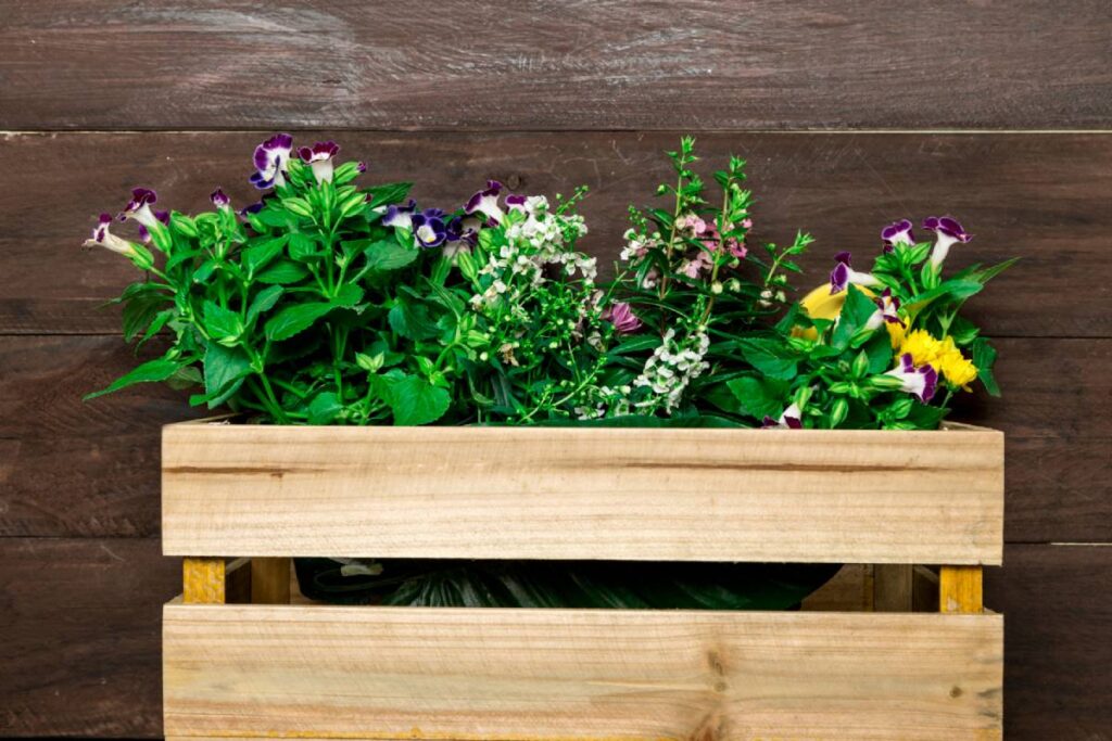 A wooden planter filled with lush green plants and colorful flowers, set against a rustic wooden backdrop.