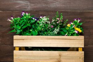 A wooden planter filled with lush green plants and colorful flowers, set against a rustic wooden backdrop.