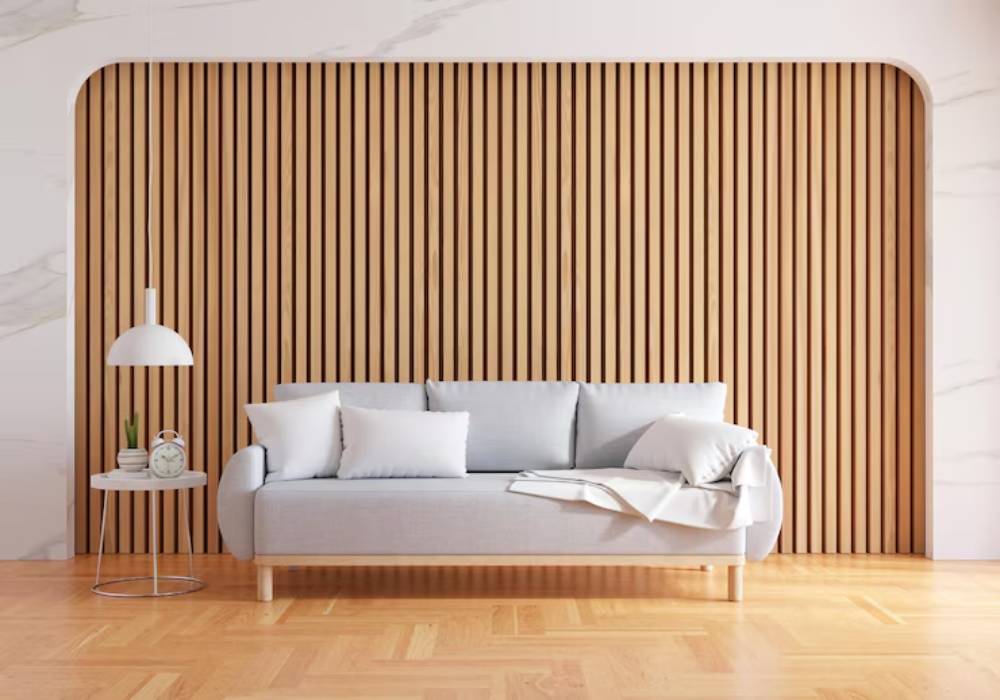 A modern, light-gray couch with cushions sits in front of a stylish wood panel, accompanied by a minimalist lamp and side table.