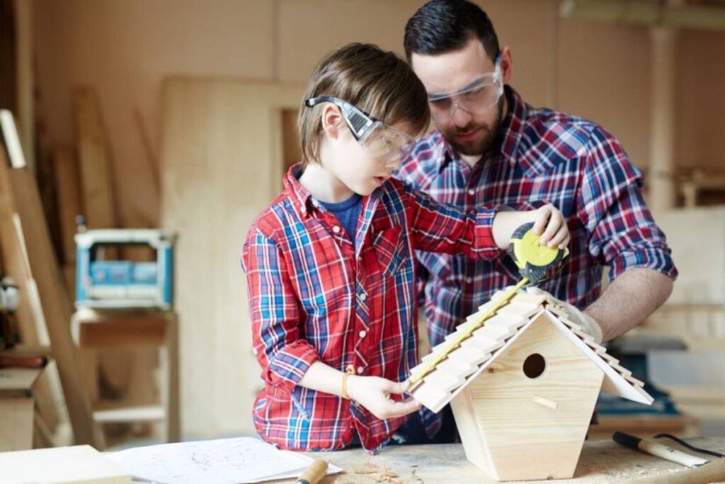 A child and adult work together to build a wooden birdhouse, using a measuring tape in a cozy workshop filled with tools.