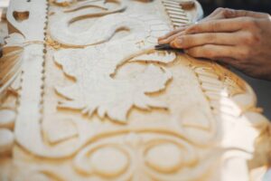 Close-up of a woodworker's hands carving intricate designs into a detailed wooden panel, showcasing craftsmanship and artistry.