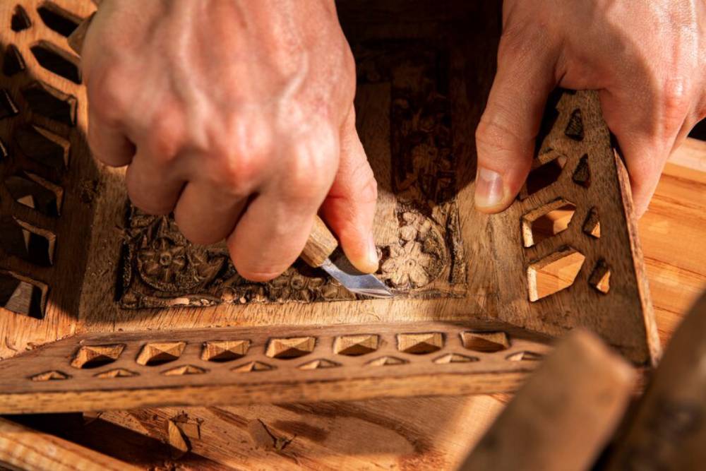 A craftsman carves intricate designs into a wooden piece, skillfully using a carving knife.