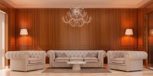 Elegant living room with beige tufted sofas, a round coffee table, and a sparkling chandelier against a warm wooden wallpanel.