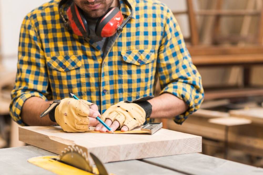 A man measures wood while wearing fingerless gloves, preparing for woodworking.